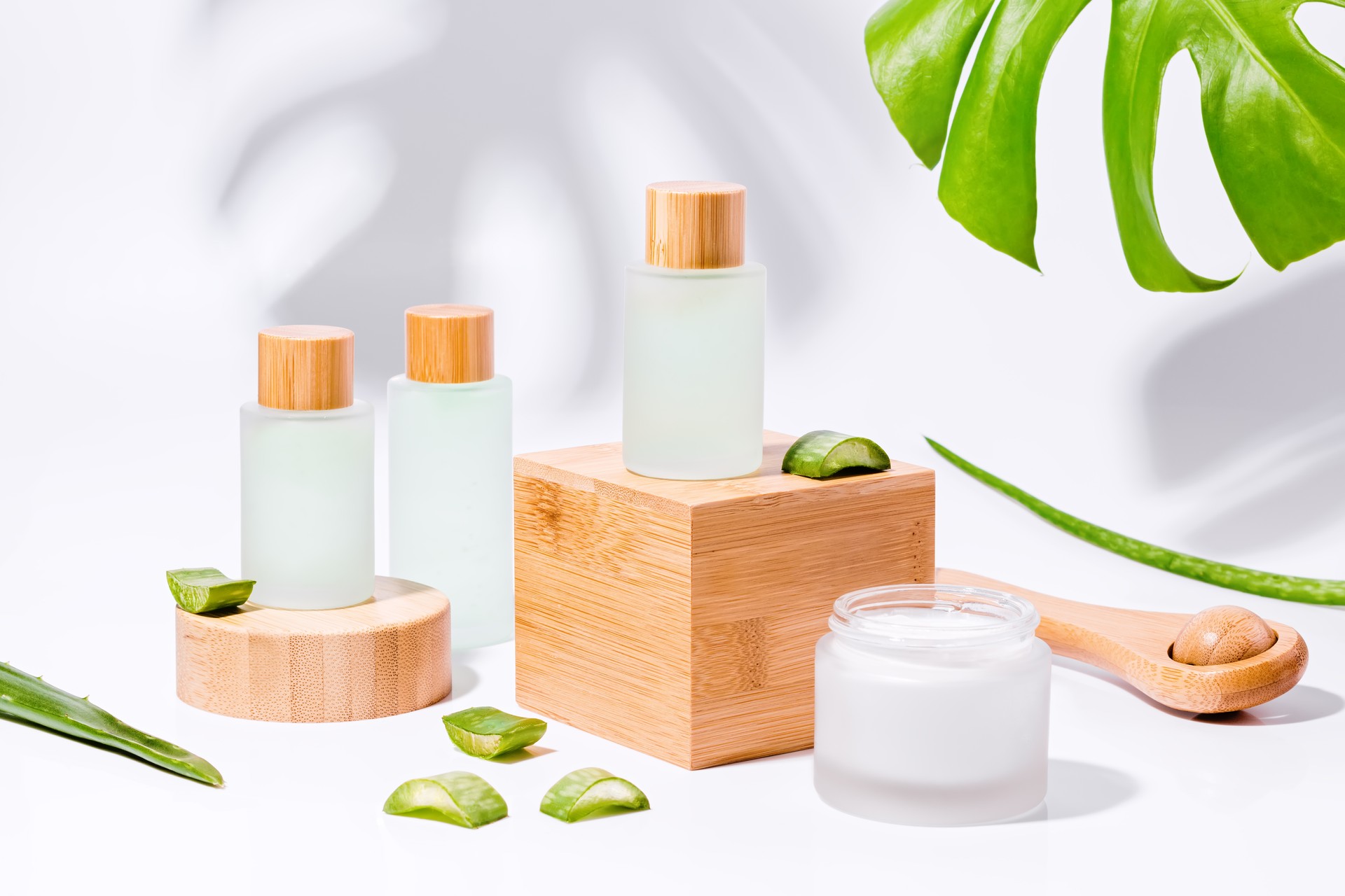 Natural cosmetics with aloe on wooden podiums in reusable bottles with plant shadow on background